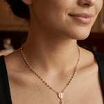 modelo con Collar tipo rosario de plata de ley 925 enchapada en oro 18k con pequeñas esferas, medalla central y dije de cruz colgante.