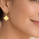 Detalle de modelo luciendo los aretes Flor VC, resaltando el brillo y el relieve del dije floral.