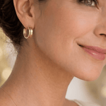 Detalle de modelo sonriendo luciendo la argolla Cinta Lineal de oro laminado en la oreja.