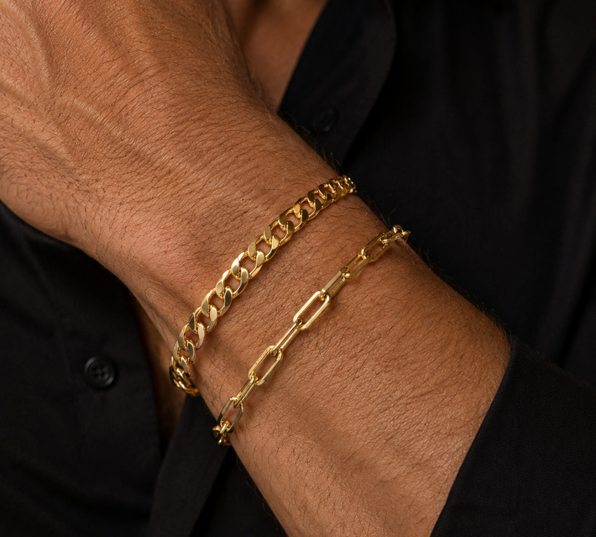Pulsera masculina de oro laminado con eslabones planos tipo Grumet lucida en la muñeca de un caballero sobre una camisa negra.