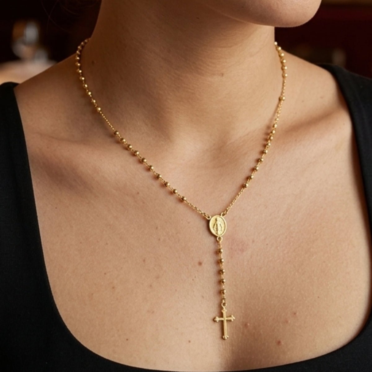 modelo con Collar tipo rosario de plata de ley 925 enchapada en oro 18k con pequeñas esferas, medalla central y dije de cruz colgante.