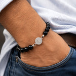 modelo con Pulsera San Benito tejida regulable con turmalina negra natural de 8 mm y accesorios de plata 950.