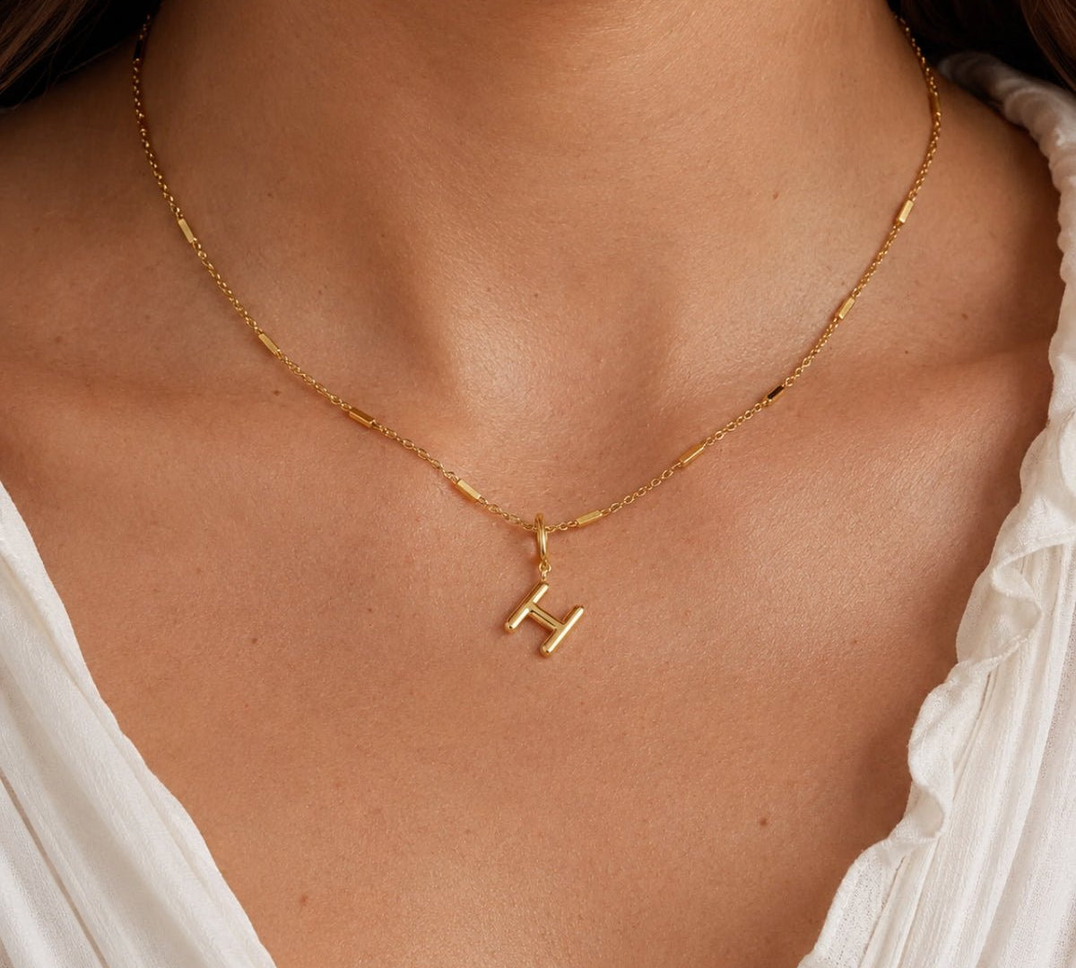 modelo luciendo Dije Inicial letra H con broche bisagra enchapado en oro 18k de AMBAR joyeria fina