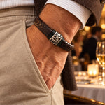 Modelo con Pulsera Cuero Trenzado Vulcano de cuero marrón con aplique central de acero inoxidable texturizado y bandas de silicona negra.