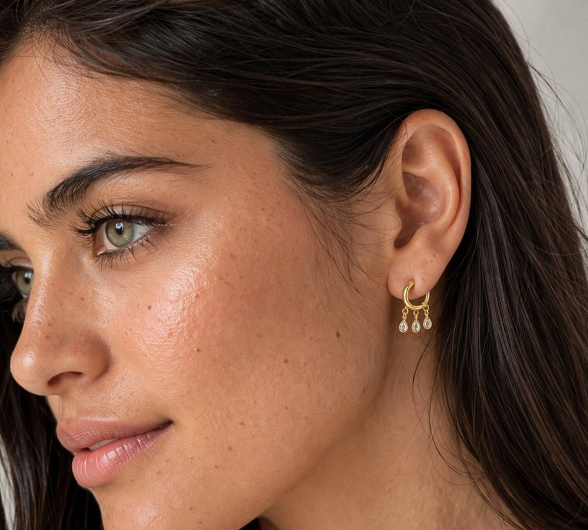 Modelo con Argollas de oro laminado con múltiples dijes colgantes de circonitas transparentes en forma de lágrima, diseño Cascada.