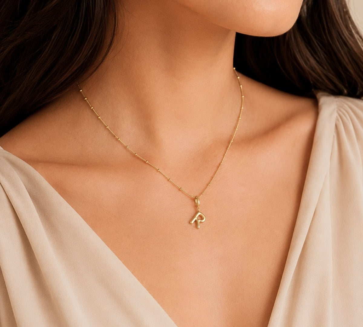 Modelo luciendo un dije Inicial letra r con broche bisagra enchapado en oro 18k de AMBAR joyería fina