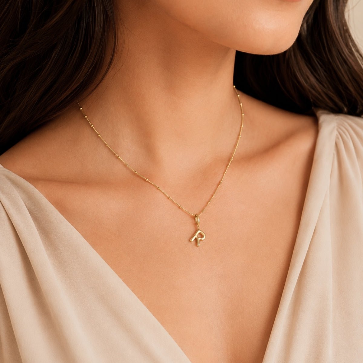 Modelo luciendo un dije Inicial letra r con broche bisagra enchapado en oro 18k de AMBAR joyería fina