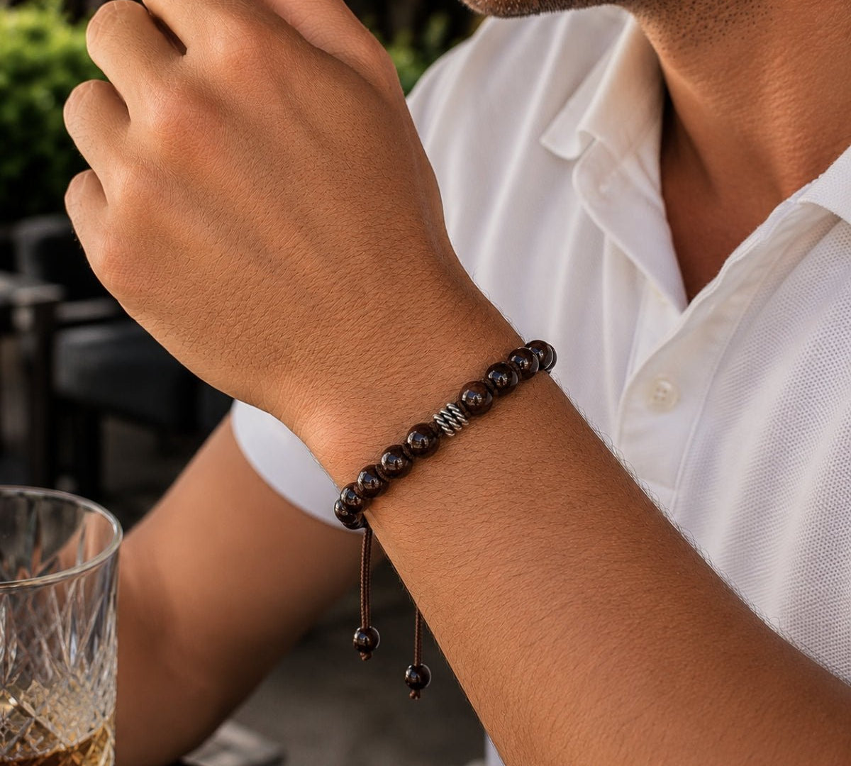 Modelo con pulsera tejida para hombre modelo Ares con hilo marrón, esferas de rodonita borgoña y tres aros de plata 925 quemada sobre fondo blanco.