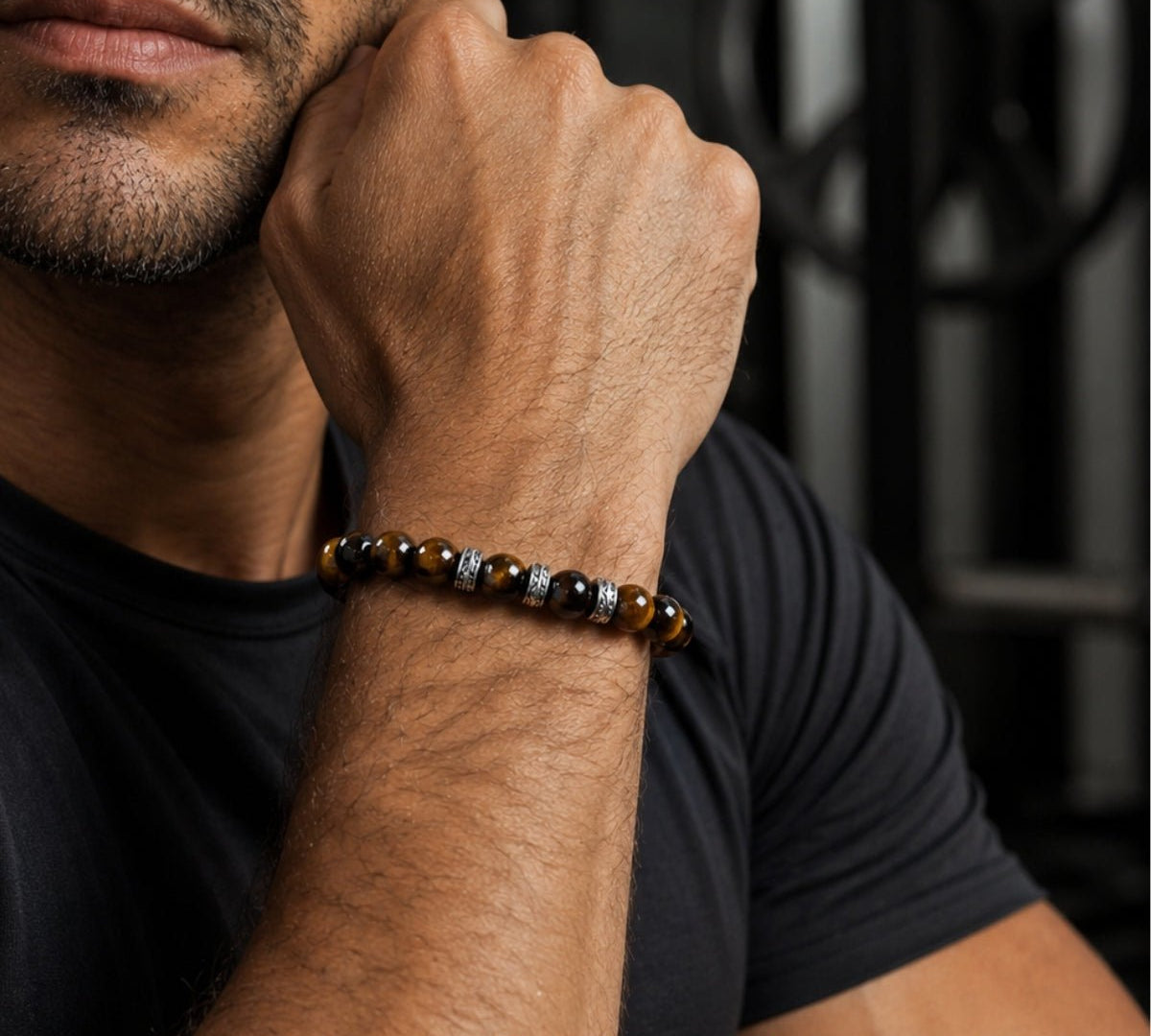 Modelo con pulsera elástica para hombre modelo Hermes con hilo de silicona, esferas ojo de tigre y tres aros texturizados de plata 925.