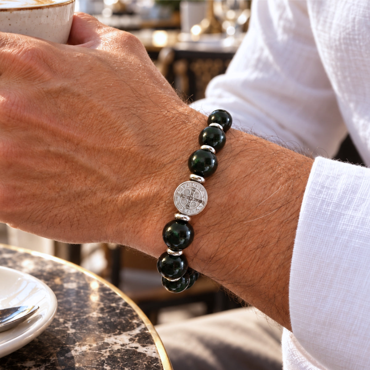 modelo con Pulsera San Benito Imperial Grand con piedras naturales de obsidiana de 10 mm, dije San Benito de acero inoxidable y donas de acero.