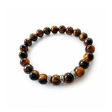 Pulsera elástica para hombre modelo Hermes con hilo de silicona, esferas de ojo de tigre y tres aros texturizados de plata 925 sobre fondo blanco.